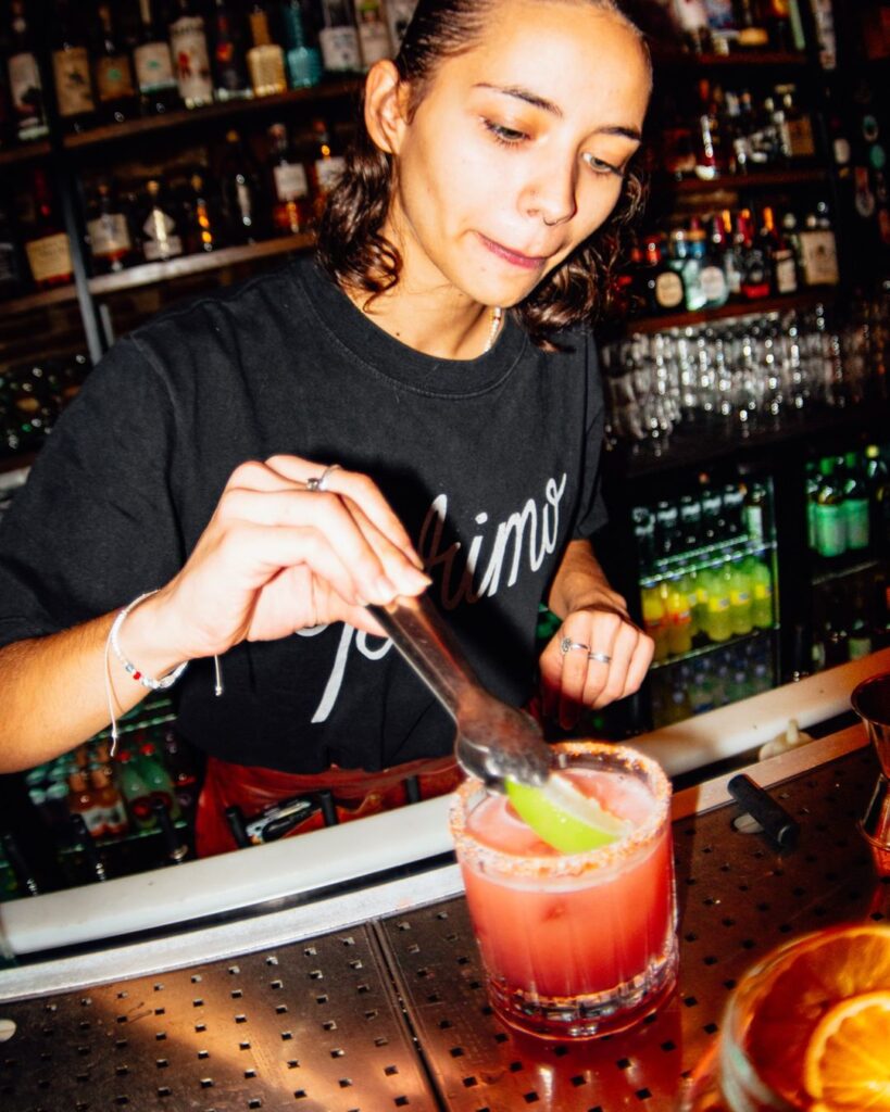 Bartender de Primo preparando un cóctel con lima en la barra, con la estantería de botellas detrás
